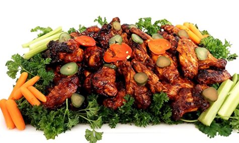 a large platter of barbecue chicken wings decorated with a variety of vegetables