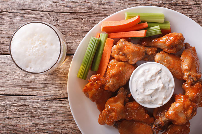 A plate of chicken wings made using Lumberjack wing sauce with celery and carrots, a dish of blue cheese and a beer